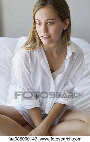 Stock Photo - Young woman sitting on bed, portrait. Fotosearch