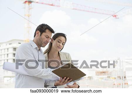 Stock Photo - Architects discussing blueprint in construction site. Fotosearch
