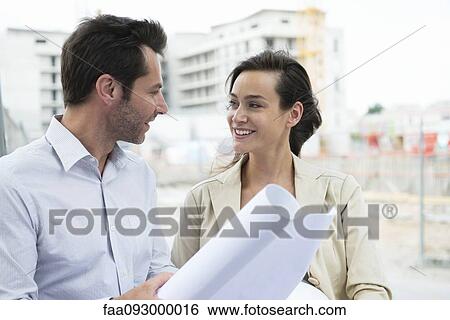 Architects discussing blueprint in construction site View Large Photo Image Stock Photograph - Architects discussing blueprint in construction site. Fotosearch
