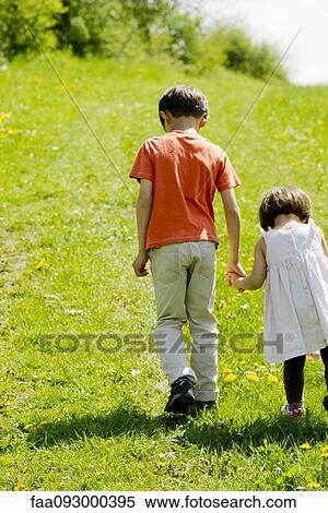Brother and sister walking hand-in-hand through field View Large Photo Image Stock Photography - Brother and sister walking hand-in-hand through field. Fotosearch