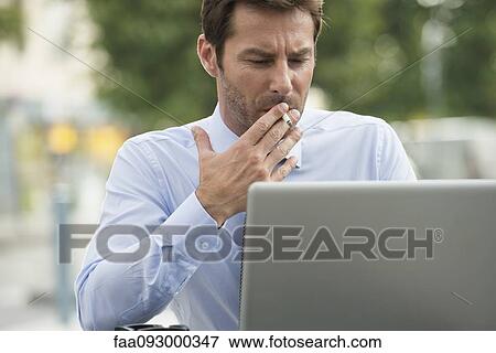 Businessman smoking while using laptop computer outdoors View Large Photo Image Stock Photo - Businessman smoking while using laptop computer outdoors. Fotosearch