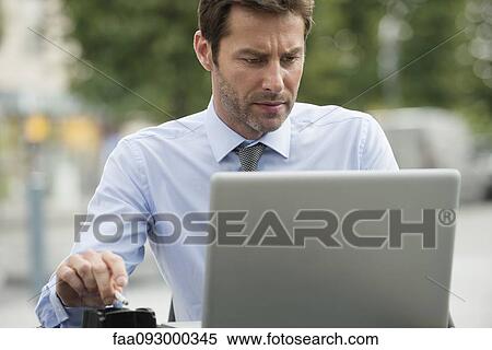 Stock Photography - Businessman smoking while using laptop computer outdoors. Fotosearch