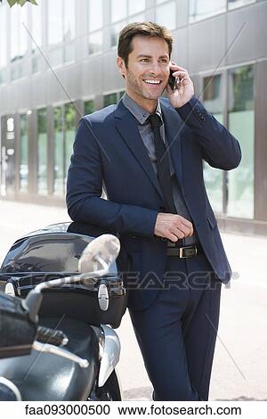 Businessman talking on cell phone in city, leaning against motor scooters View Large Photo Image Stock Image - Businessman talking on cell phone in city, leaning against motor scooters. Fotosearch