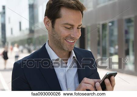 Stock Photograph - Businessman using smartphone outdoors. Fotosearch