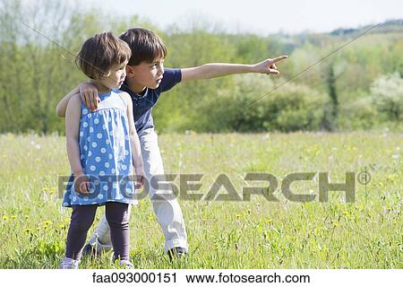 Stock Image - Children standing in field together, looking at something in the distance. Fotosearch