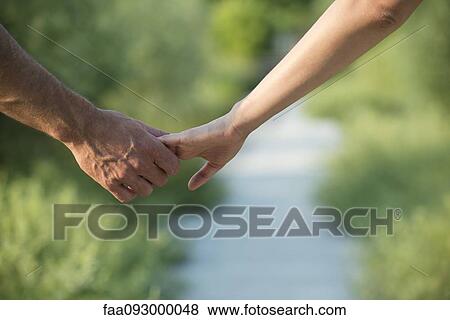 Stock Photo - Couple hesitantly hold hands, close-up. Fotosearch
