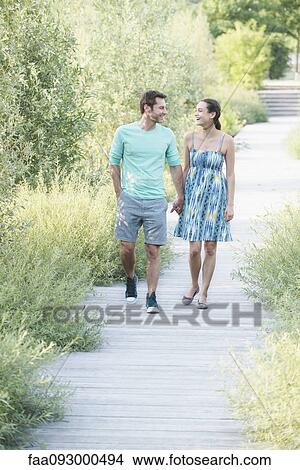 Couple holding hands enjoying walk along boardwalk through nature preserve View Large Photo Image Picture - Couple holding hands enjoying walk along boardwalk through nature preserve. Fotosearch