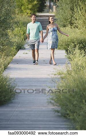 Couple holding hands enjoying walk along boardwalk through nature preserve View Large Photo Image Stock Image - Couple holding hands enjoying walk along boardwalk through nature preserve. Fotosearch