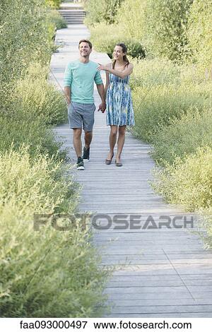 Stock Photo - Couple holding hands enjoying walk along boardwalk through nature preserve. Fotosearch