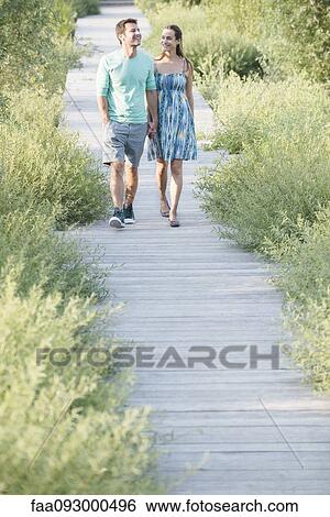 Couple holding hands enjoying walk along boardwalk through nature preserve View Large Photo Image Stock Photograph - Couple holding hands enjoying walk along boardwalk through nature preserve. Fotosearch
