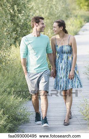 Stock Photography - Couple holding hands enjoying walk along boardwalk through nature preserve. Fotosearch