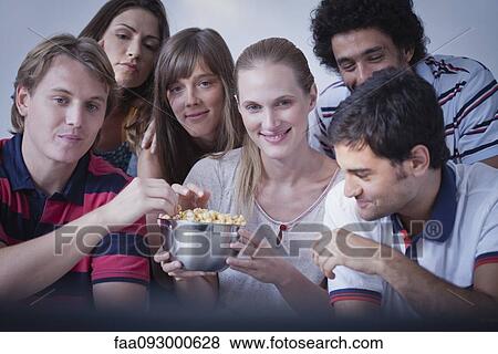 Stock Photo - Friends sharing popcorn and watching movie together. Fotosearch
