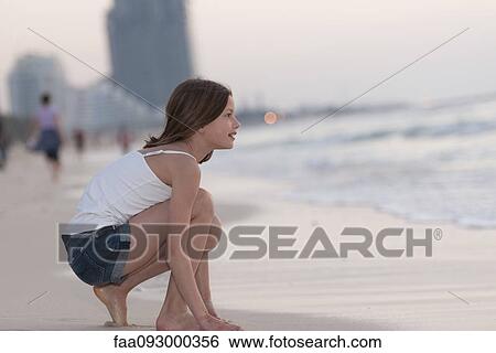 Girl crouching on beach, looking at water View Large Photo Image Stock Photograph - Girl crouching on beach, looking at water. Fotosearch