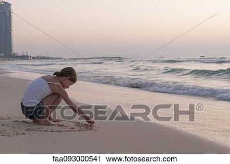 Stock Image - Girl drawing in sand on beach. Fotosearch