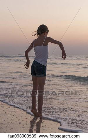Stock Photo - Girl playing on beach, rear view. Fotosearch