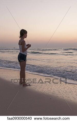 Stock Image - Girl standing on beach looking at sea. Fotosearch