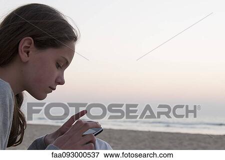 Stock Photo - Girl using smartphone on beach, side view. Fotosearch