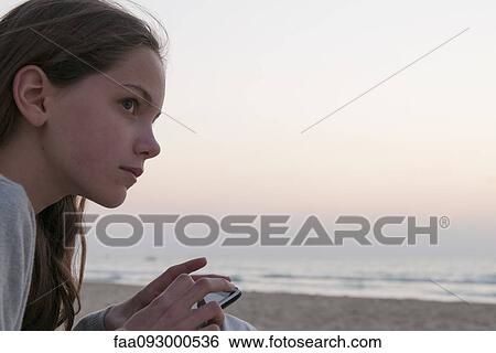 Stock Photograph - Girl using smartphone on beach, side view. Fotosearch