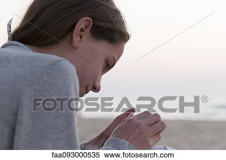 Stock Photography - Girl using smartphone on beach, side view. Fotosearch