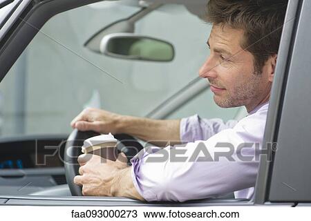 Stock Image - Man driving car with cup of coffee in one hand. Fotosearch