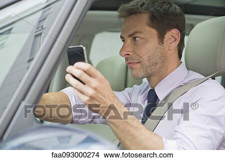 Picture - Man using smartphone while driving. Fotosearch