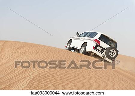 Picture - Sports utility vehicle driving up desert sand dune. Fotosearch