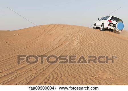 Stock Photo - Sports utility vehicle driving up desert sand dune. Fotosearch