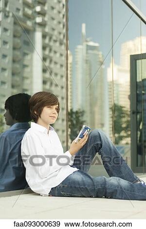 Teenage boy sitting on ground reading guidebook View Large Photo Image Stock Photo - Teenage boy sitting on ground reading guidebook. Fotosearch