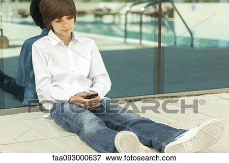 Stock Photo - Teenage boy sitting on ground using cell phone. Fotosearch