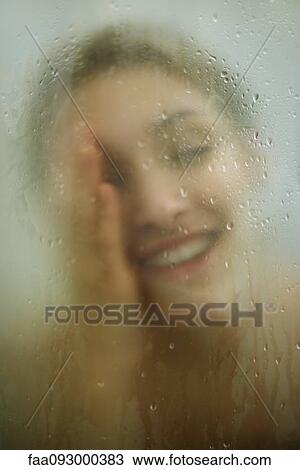 Stock Image - Woman behind shower door, wiping face. Fotosearch