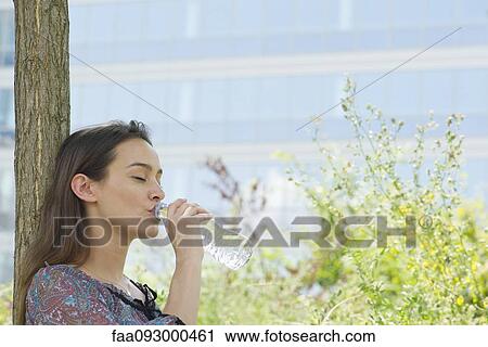 Stock Image - Woman drinking bottled water outdoors. Fotosearch