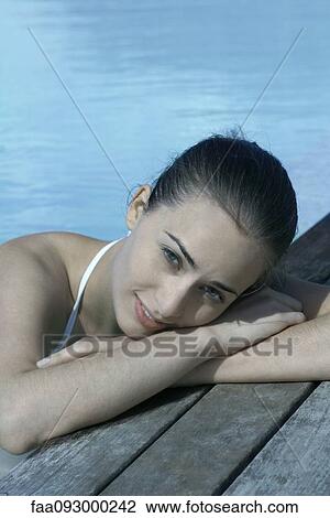 Stock Image - Woman in pool leaning against deck, resting head on arms. Fotosearch
