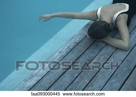 Woman in swimsuit lying on deck next to swimming pool, touching surface of water with hand View Large Photo Image Stock Photography - Woman in swimsuit lying on deck next to swimming pool, touching surface of water with hand. Fotosearch