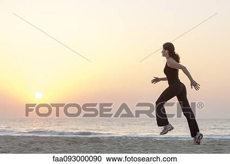 Woman jogging on beach at sunrise with earphones, side view View Large Photo Image Stock Image - Woman jogging on beach at sunrise with earphones, side view. Fotosearch