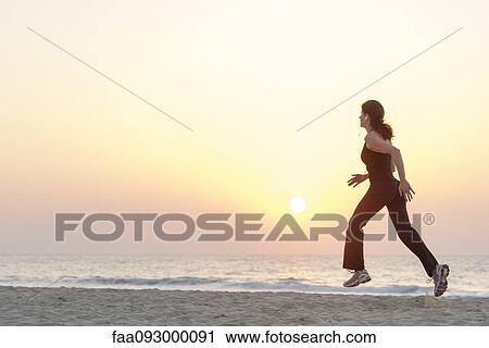 Woman jogging on beach at sunrise with earphones View Large Photo Image Stock Image - Woman jogging on beach at sunrise with earphones. Fotosearch