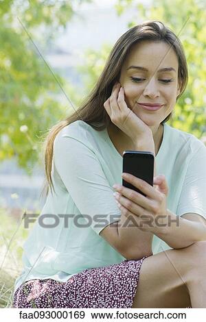 Stock Photo - Woman looking at smartphone outdoors. Fotosearch