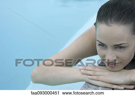 Stock Image - Woman lying next to pool, resting head on arms, looking away. Fotosearch