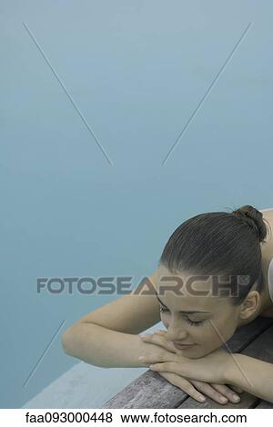 Stock Photo - Woman lying next to pool, resting head on arms, eyes closed. Fotosearch