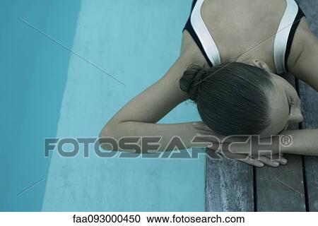 Stock Image - Woman lying on deck next to pool, resting head on arms. Fotosearch