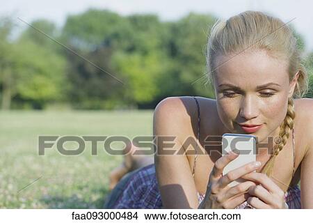 Woman lying on grass using smartphone View Large Photo Image Picture - Woman lying on grass using smartphone. Fotosearch
