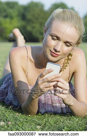 Woman lying on grass, using smartphone View Large Photo Image Stock Photo - Woman lying on grass, using smartphone. Fotosearch
