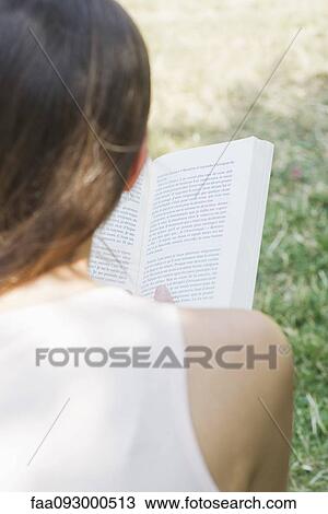 Stock Image - Woman reading book outdoors, over the shoulder view. Fotosearch