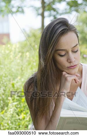 Stock Image - Woman reading book outdoors. Fotosearch