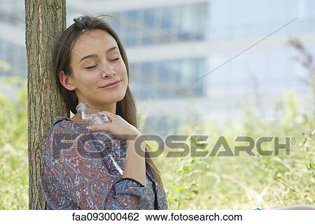 Woman relaxing outdoors with water bottle, eyes closed View Large Photo Image Stock Image - Woman relaxing outdoors with water bottle, eyes closed. Fotosearch