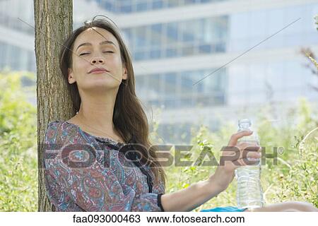 Woman relaxing outdoors with water bottle, eyes closed View Large Photo Image Stock Image - Woman relaxing outdoors with water bottle, eyes closed. Fotosearch