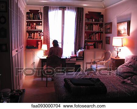 Picture - Woman sitting at desk in bedroom, rear view. Fotosearch