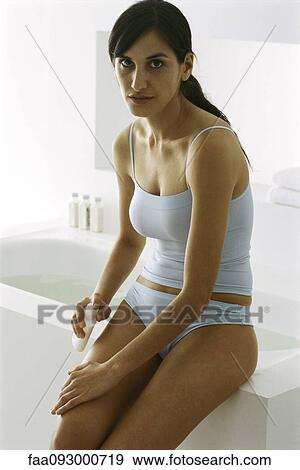 Woman sitting on edge of bathtub, putting moisturizer on leg, looking at camera View Large Photo Image Stock Photo - Woman sitting on edge of bathtub, putting moisturizer on leg, looking at camera. Fotosearch