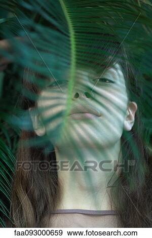 Stock Photo - Woman standing behind leaves, looking at camera, low angle view. Fotosearch