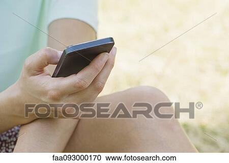 Stock Image - Woman using smartphone outdoors, cropped. Fotosearch