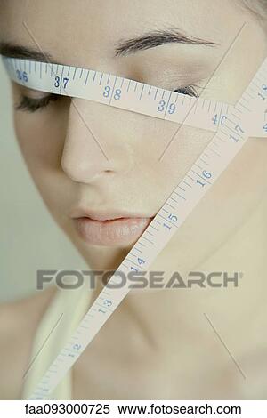 Stock Photography - Woman with measuring tape wrapped across face, eyes closed. Fotosearch